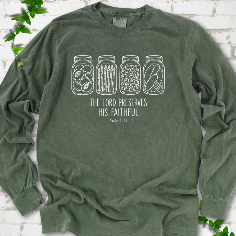 Hemp long sleeve T-shirt flat lay with white line-art illustrations of four mason jars filled with peaches, asparagus, blueberries and pickles above the words "The Lord Preserves His Faithful" and small "Psalm 31:23", on white brick with ivy sprigs.