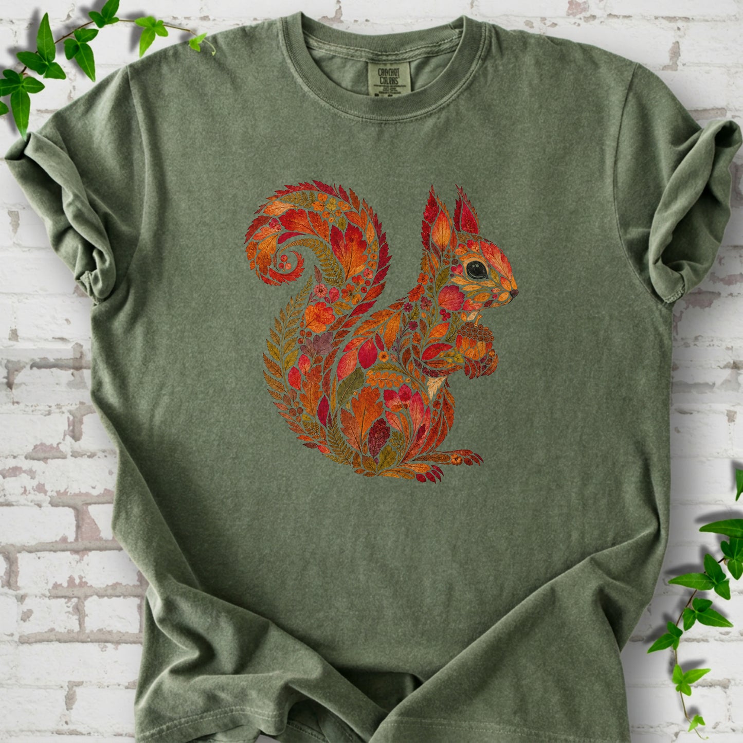 Ivory Comfort Colors® T-shirt flat lay with an autumn squirrel graphic made from colorful leaves, ferns and flowers.