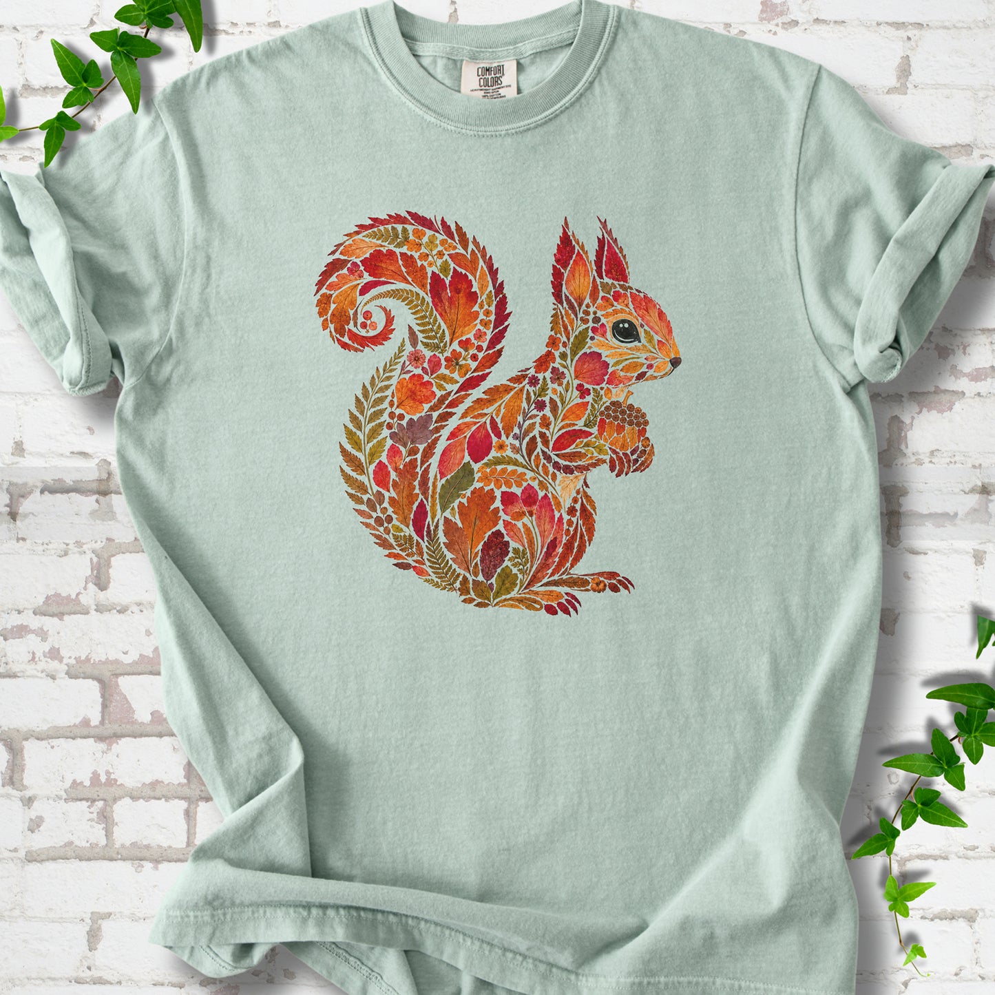 Moss Comfort Colors® T-shirt flat lay with an autumn squirrel graphic made from colorful leaves, ferns and flowers.