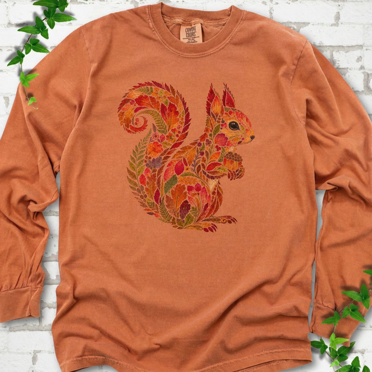 Hemp Comfort Colors® long sleeve T-shirt flat lay with an autumn squirrel graphic made from colorful leaves, ferns and flowers.