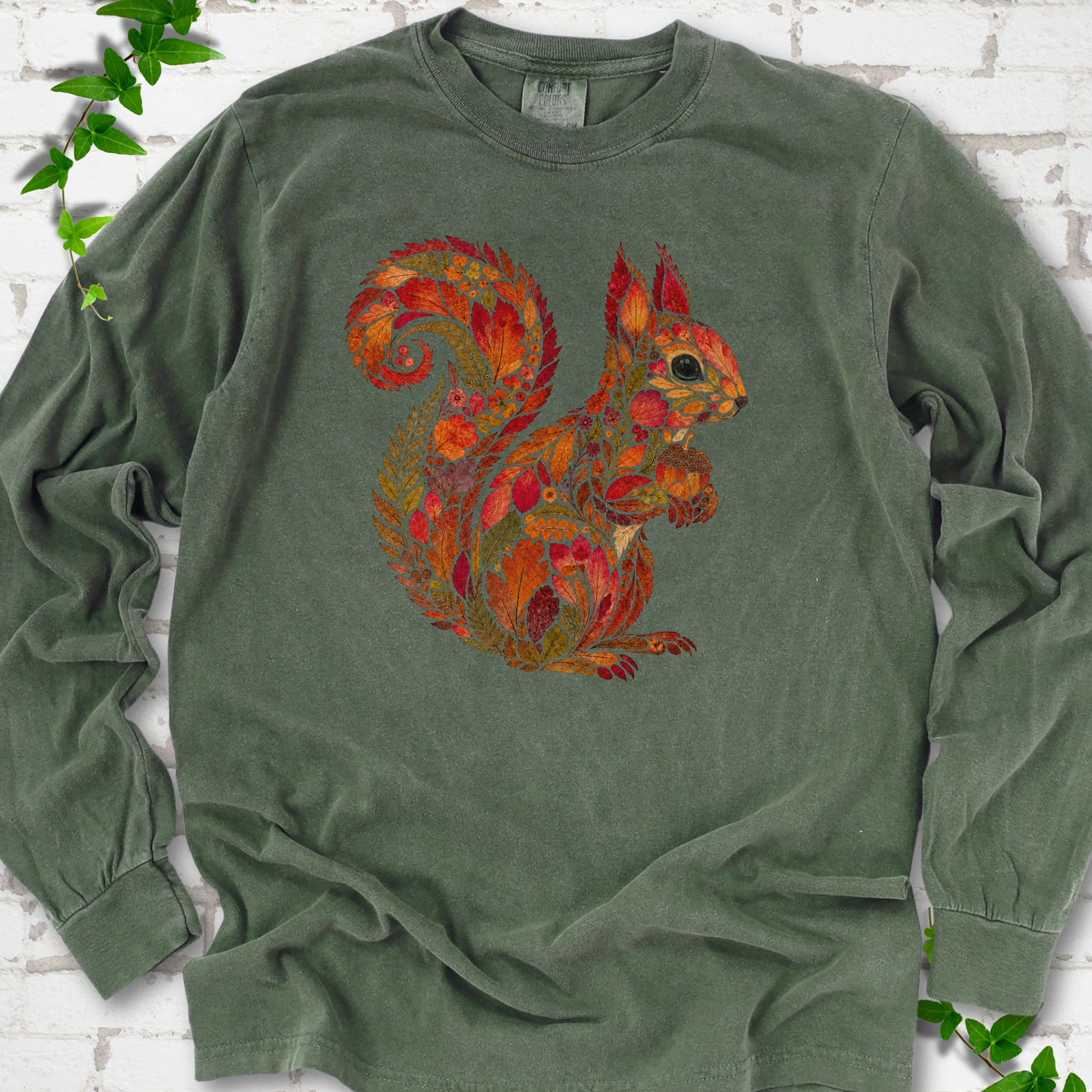Ivory Comfort Colors® long sleeve T-shirt flat lay with an autumn squirrel graphic made from colorful leaves, ferns and flowers.