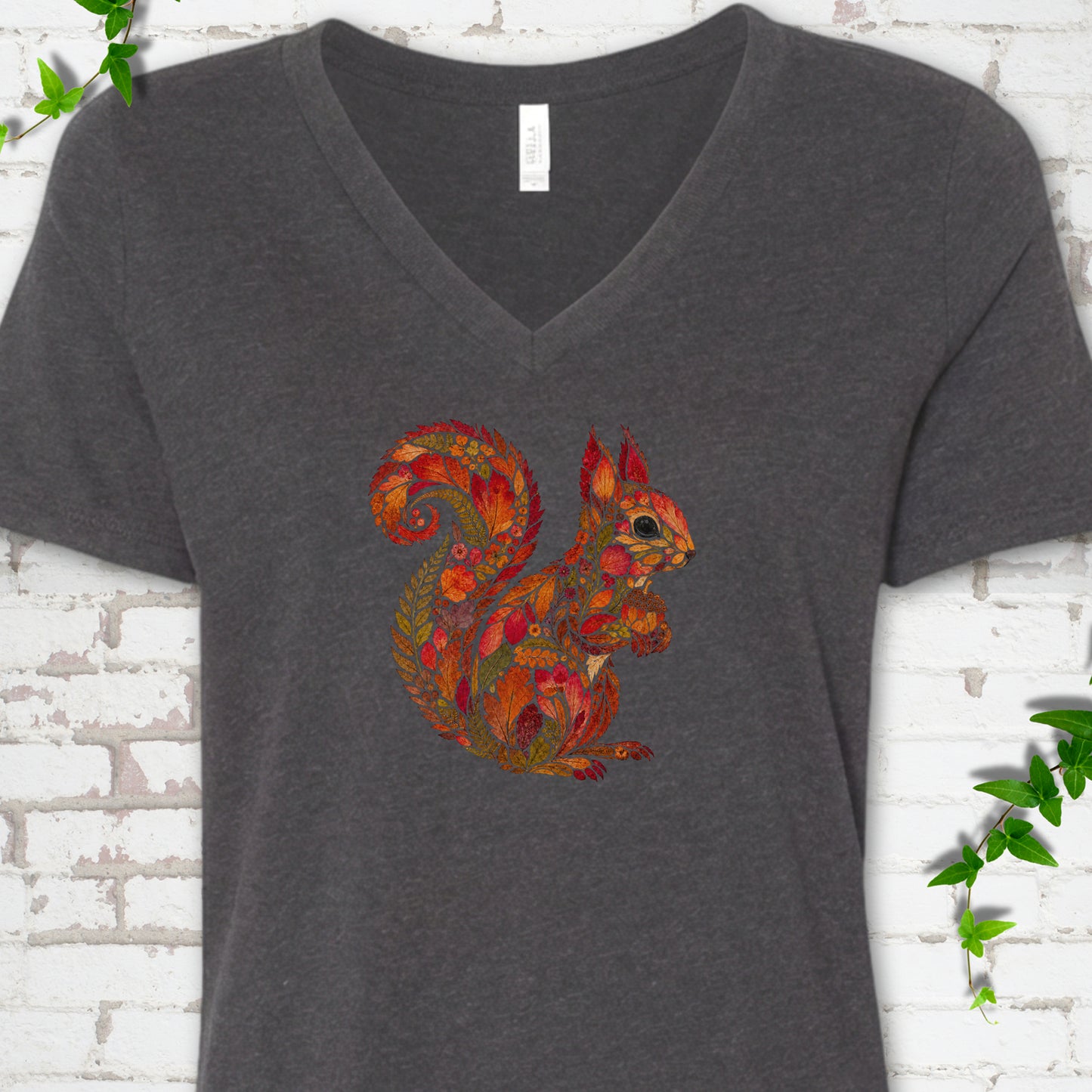 Heather Peach Bella Canvas® V-neck T-shirt flat lay with an autumn squirrel graphic made from colorful leaves, ferns and flowers.