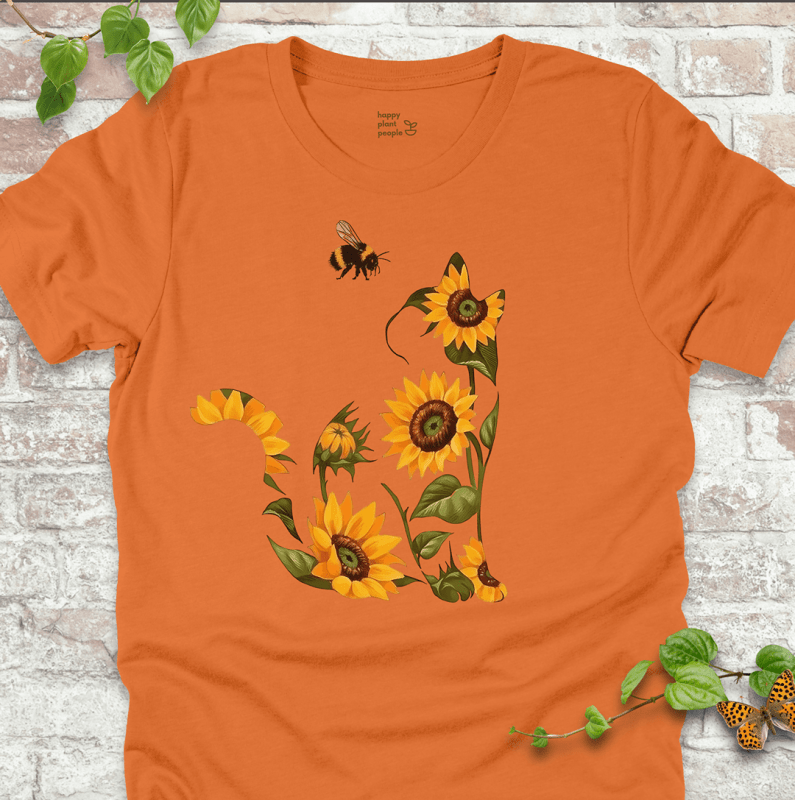 Cute T-shirt in orange with a floral cat design made of sunflowers and a bee. Cozy fall garden-themed shirt for plant lovers and cat fans.