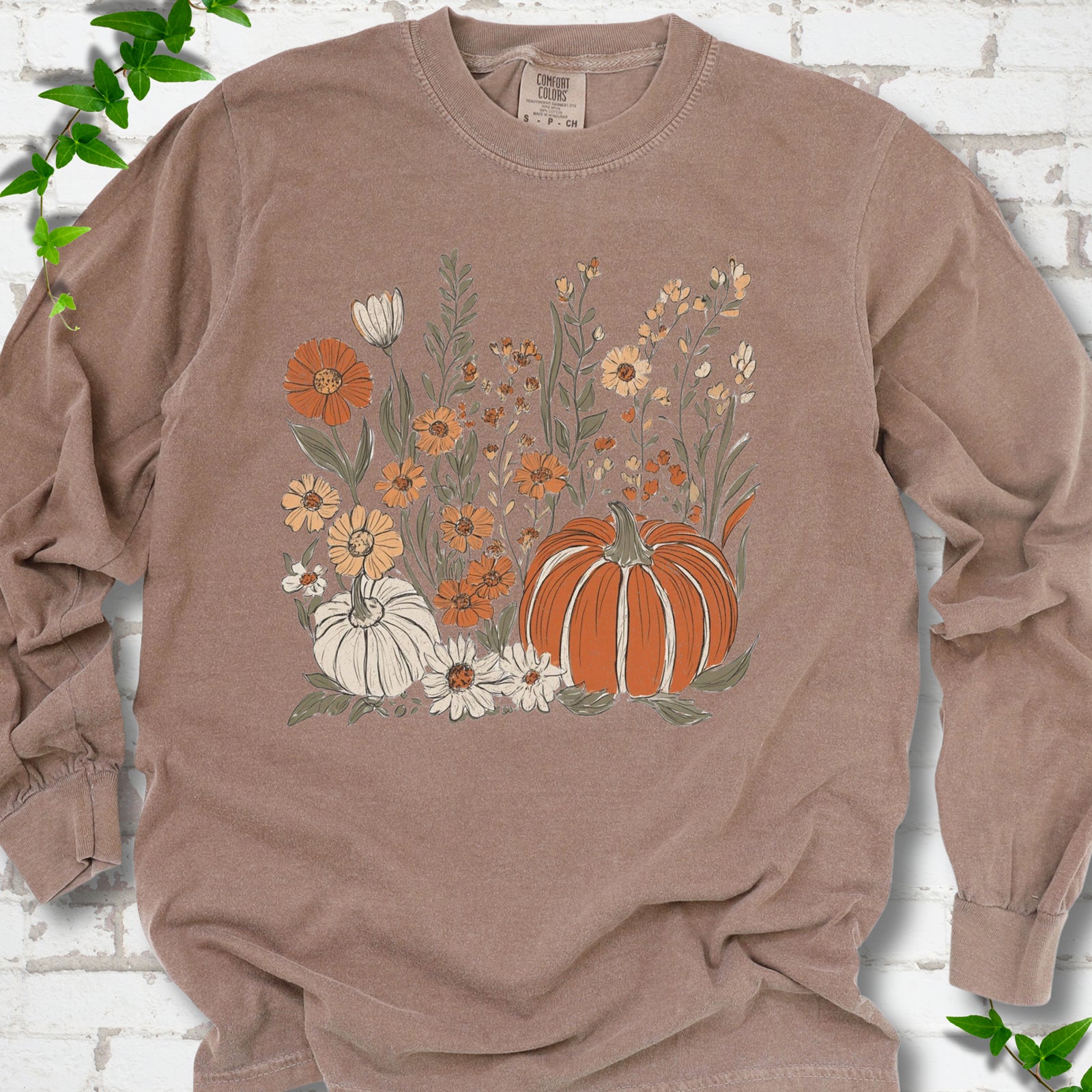 Espresso Comfort Colors® long sleeve T-shirt flat lay featuring an orange pumpkin surrounded by cream and orange wildflowers.