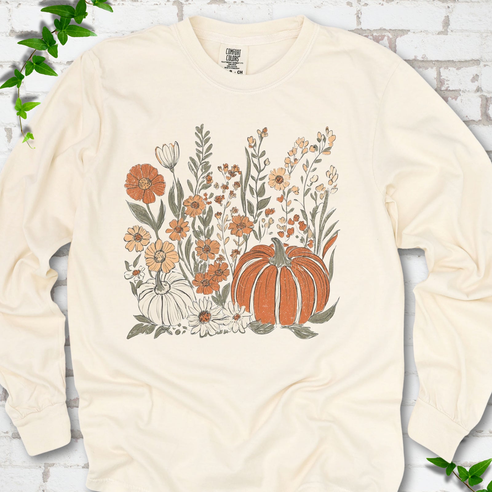 Ivory Comfort Colors® long sleeve T-shirt flat lay featuring an orange pumpkin surrounded by cream and orange wildflowers.