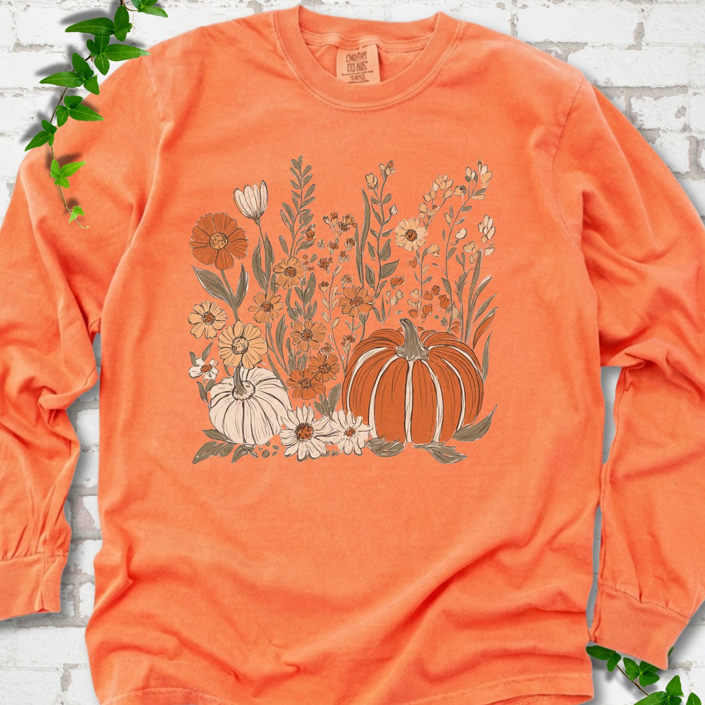 Melon Comfort Colors® long sleeve T-shirt flat lay featuring an orange pumpkin surrounded by cream and orange wildflowers.