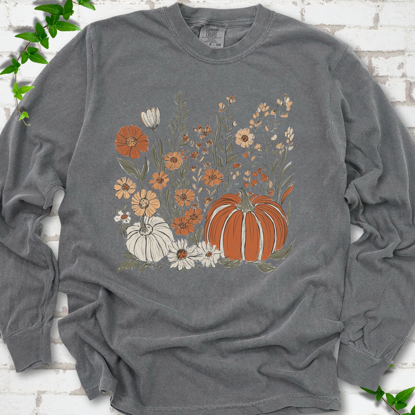 Pepper Comfort Colors® long sleeve T-shirt flat lay featuring an orange pumpkin surrounded by cream and orange wildflowers.