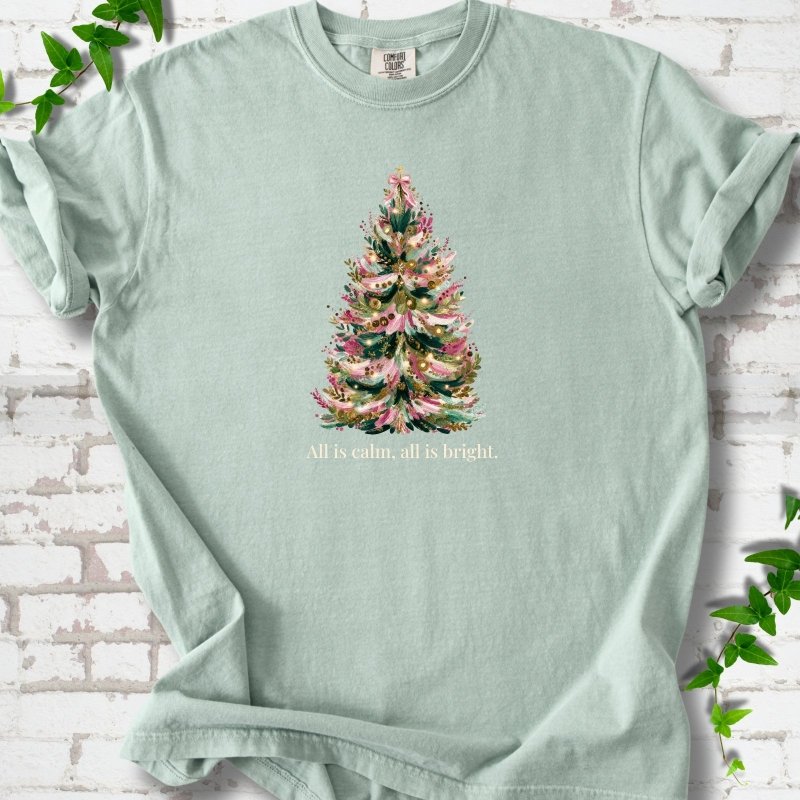 Bay T-shirt laid flat, featuring a decorated evergreen tree with pink ribbon garlands, a pink bow and gold ornaments above the words 'All is calm, all is bright.'