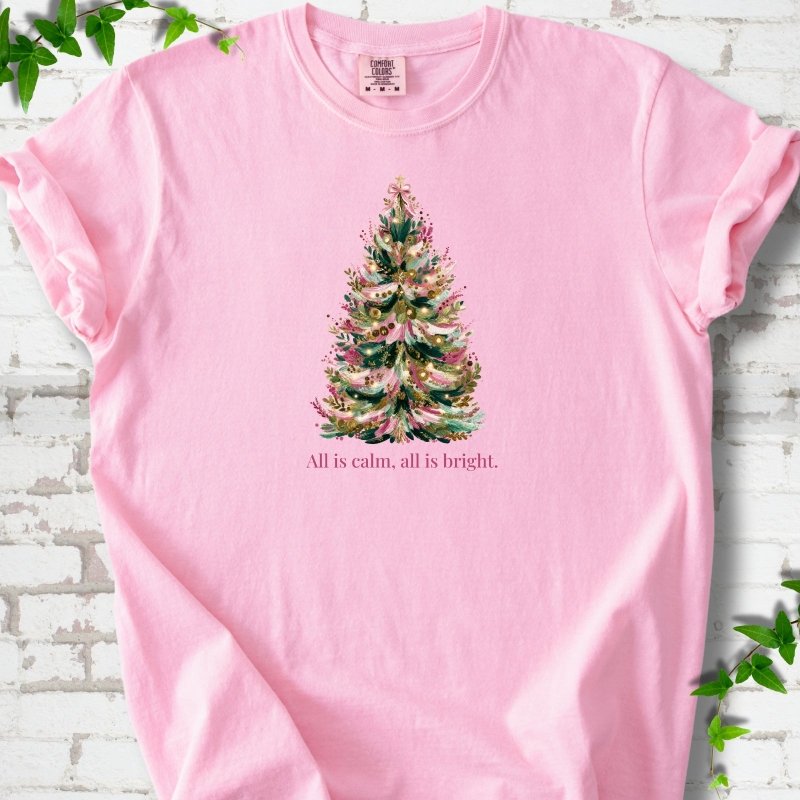 Blossom T-shirt laid flat, featuring a decorated evergreen tree with pink ribbon garlands, a pink bow and gold ornaments above the words 'All is calm, all is bright.'
