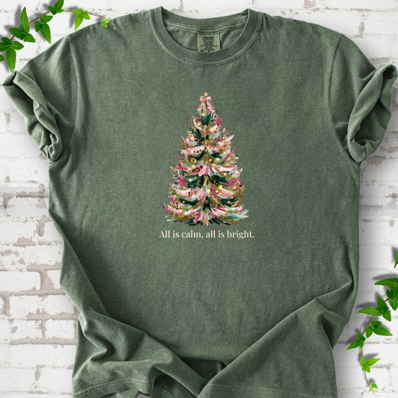 Hemp T-shirt laid flat, featuring a decorated evergreen tree with pink ribbon garlands, a pink bow and gold ornaments above the words 'All is calm, all is bright.'