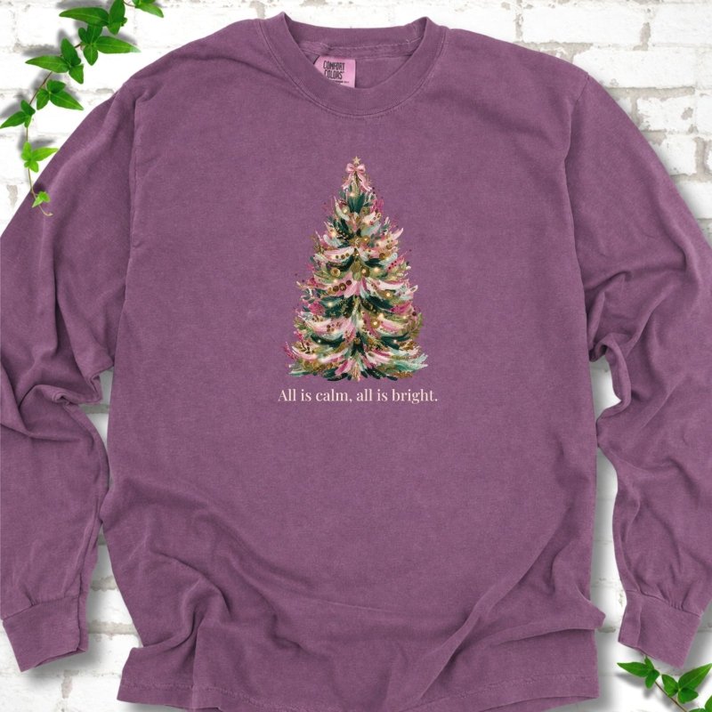 Berry long sleeve T-shirt laid flat, featuring a decorated evergreen tree with pink ribbon garlands, a pink bow and gold ornaments above the words 'All is calm, all is bright.'