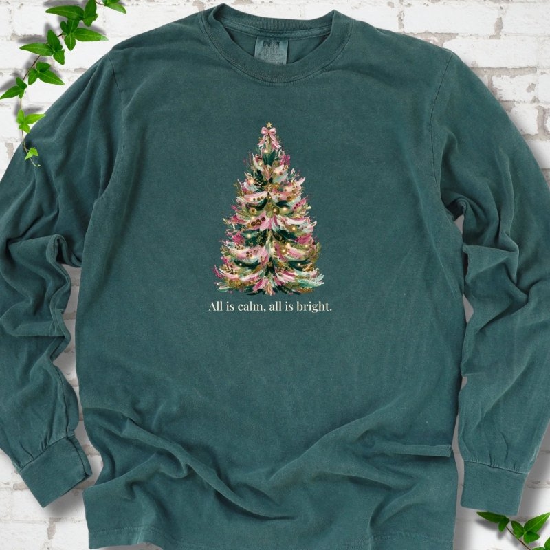Blue Spruce long sleeve T-shirt laid flat, featuring a decorated evergreen tree with pink ribbon garlands, a pink bow and gold ornaments above the words 'All is calm, all is bright.'