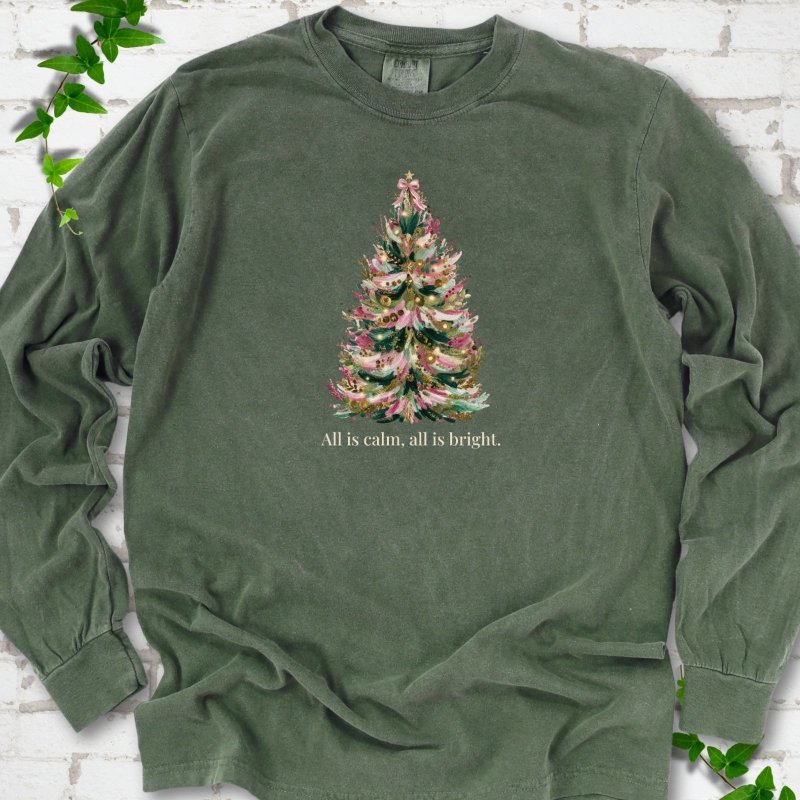 Hemp long sleeve T-shirt laid flat, featuring a decorated evergreen tree with pink ribbon garlands, a pink bow and gold ornaments above the words 'All is calm, all is bright.'