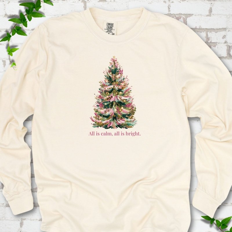 Ivory long sleeve T-shirt laid flat, featuring a decorated evergreen tree with pink ribbon garlands, a pink bow and gold ornaments above the words 'All is calm, all is bright.'