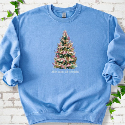 Carolina Blue sweatshirt laid flat, featuring a decorated evergreen tree with pink ribbon garlands, a pink bow and gold ornaments above the words 'All is calm, all is bright.'