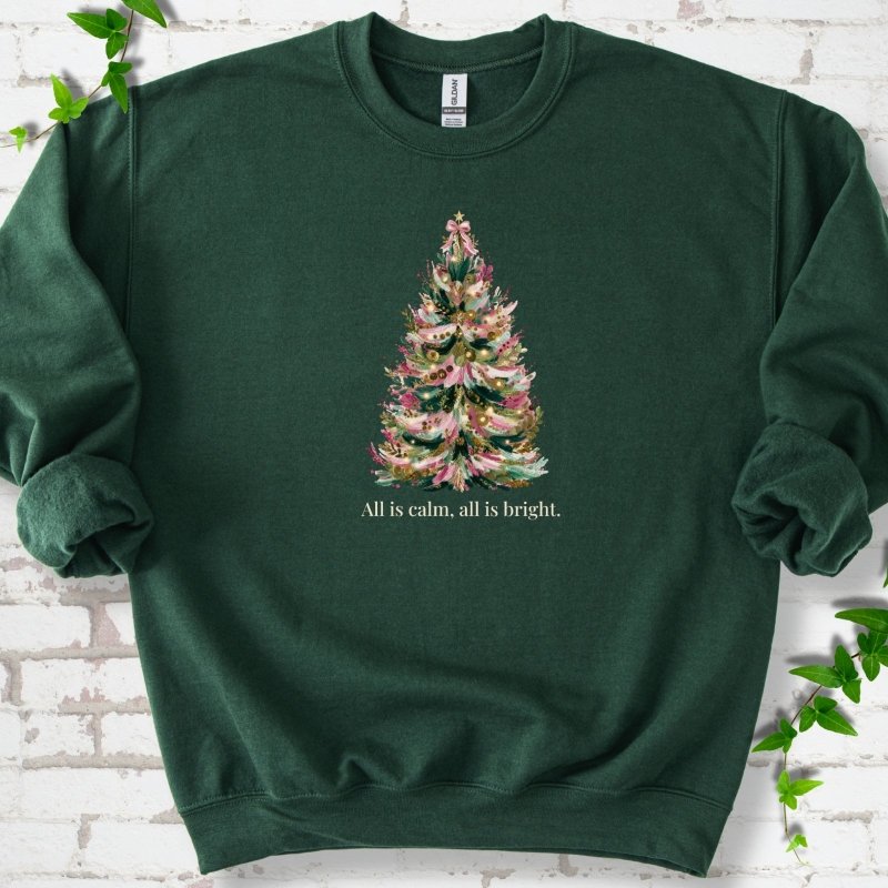 Forest Green sweatshirt laid flat, featuring a decorated evergreen tree with pink ribbon garlands, a pink bow and gold ornaments above the words 'All is calm, all is bright.'