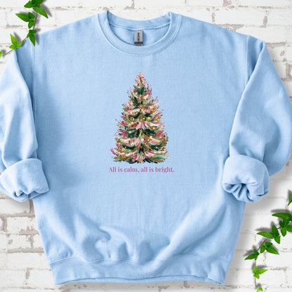 Light Blue sweatshirt laid flat, featuring a decorated evergreen tree with pink ribbon garlands, a pink bow and gold ornaments above the words 'All is calm, all is bright.'