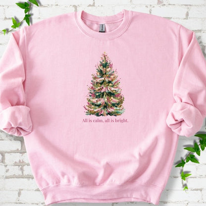 Light Pink sweatshirt laid flat, featuring a decorated evergreen tree with pink ribbon garlands, a pink bow and gold ornaments above the words 'All is calm, all is bright.'