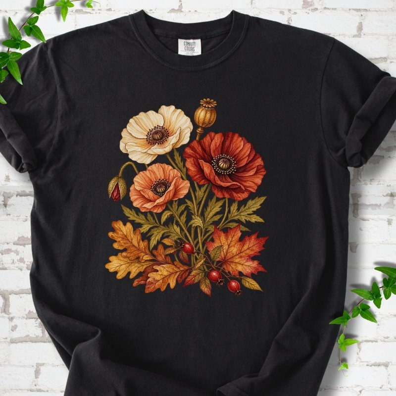 Black short sleeve t-shirt with a botanical bouquet of cream, peach and deep red poppies with a seed pod, oak and maple leaves and red rose hips, printed on the chest, flat lay on white brick with ivy