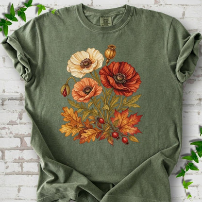 Moss green short sleeve t-shirt with a botanical bouquet of cream, peach and deep red poppies with a seed pod, oak and maple leaves and red rose hips, printed on the chest, flat lay on white brick with ivy