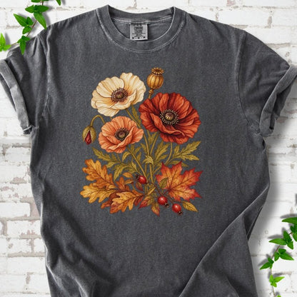Pepper charcoal gray short sleeve t-shirt with a botanical bouquet of cream, peach and deep red poppies with a seed pod, oak and maple leaves and red rose hips, printed on the chest, flat lay on white brick with ivy