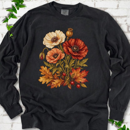 Black long sleeve t-shirt with a botanical bouquet of cream, peach and deep red poppies with a seed pod, oak and maple leaves and red rose hips, printed on the chest, flat lay on white brick with ivy