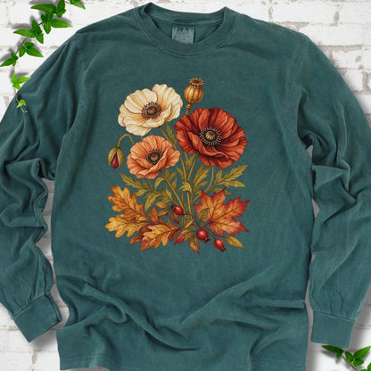 Blue Spruce deep teal long sleeve t-shirt with a botanical bouquet of cream, peach and deep red poppies with a seed pod, oak and maple leaves and red rose hips, printed on the chest, flat lay on white brick with ivy