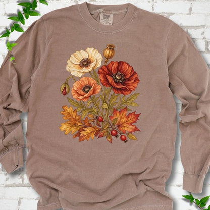 Espresso brown long sleeve t-shirt with a botanical bouquet of cream, peach and deep red poppies with a seed pod, oak and maple leaves and red rose hips, printed on the chest, flat lay on white brick with ivy