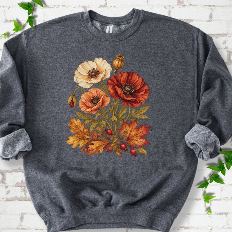 Dark Heather gray crewneck sweatshirt with a botanical bouquet of cream, peach and deep red poppies with a seed pod, oak and maple leaves and red rose hips, printed on the chest, flat lay on white brick with ivy