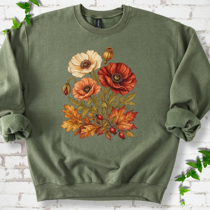 Military olive green crewneck sweatshirt with a botanical bouquet of cream, peach and deep red poppies with a seed pod, oak and maple leaves and red rose hips, printed on the chest, flat lay on white brick with ivy