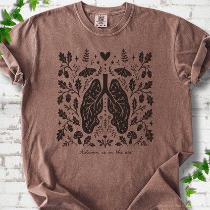 Espresso Comfort Colors® T-shirt front mockup featuring a dark, symmetrical folk-botanical graphic centered on stylized human lungs and branching airways. The lungs are framed by leafy branches, acorns, two mushrooms.