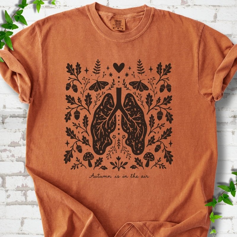 Yam Comfort Colors® T-shirt front mockup featuring a dark, symmetrical folk-botanical graphic centered on stylized human lungs and branching airways. The lungs are framed by leafy branches, acorns, two mushrooms.