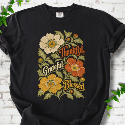 Black T-shirt flat-lay mockup with orange, cream and yellow flowers framing "Thankful, Grateful, Blessed" lettering.