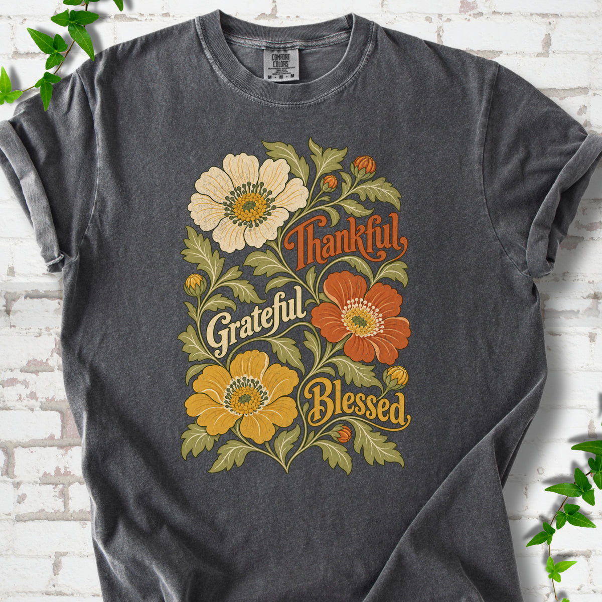 Pepper T-shirt flat-lay mockup with orange, cream and yellow flowers framing "Thankful, Grateful, Blessed" lettering.