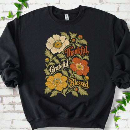 Black sweatshirt flat-lay mockup with orange, cream and yellow flowers framing "Thankful, Grateful, Blessed" lettering.