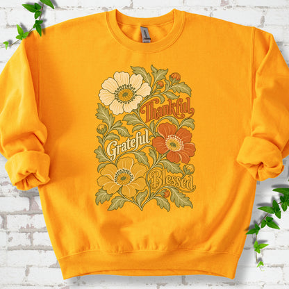 Gold sweatshirt flat-lay mockup with orange, cream and yellow flowers framing "Thankful, Grateful, Blessed" lettering.