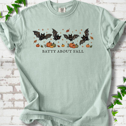 Bay Comfort Colors® T-shirt flat lay featuring four black bats above pumpkins and autumn leaves with “Batty About Fall” lettering.