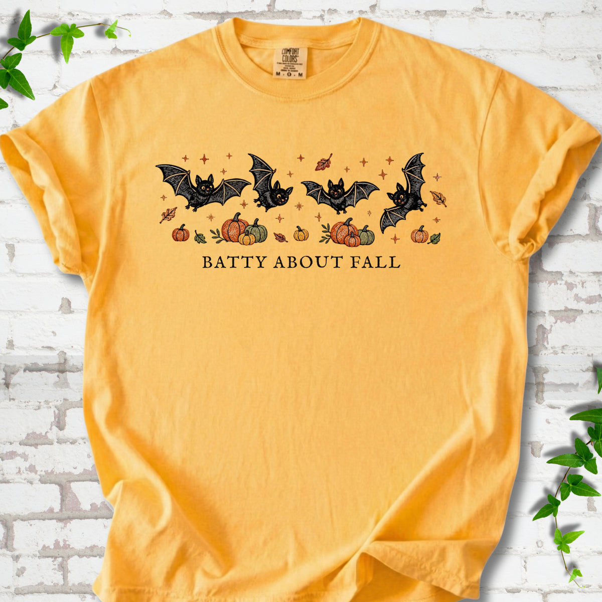Citrus Comfort Colors® T-shirt flat lay featuring four black bats above pumpkins and autumn leaves with “Batty About Fall” lettering.