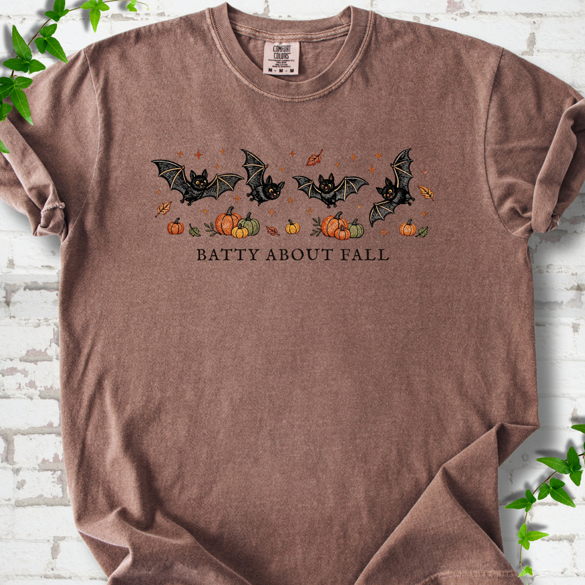 Espresso Comfort Colors® T-shirt flat lay featuring four black bats above pumpkins and autumn leaves with “Batty About Fall” lettering.