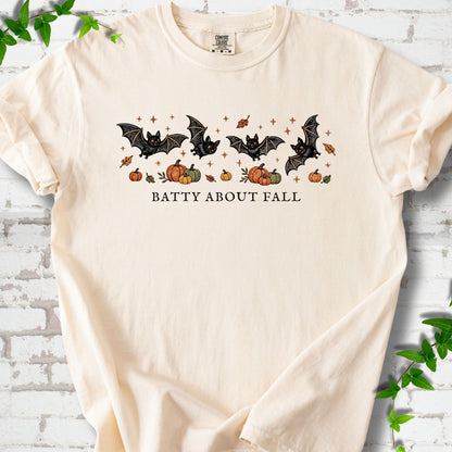 Ivory Comfort Colors® T-shirt flat lay featuring four black bats above pumpkins and autumn leaves with “Batty About Fall” lettering.
