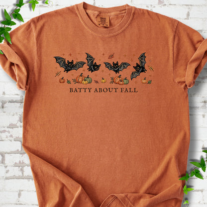 Yam Comfort Colors® T-shirt flat lay featuring four black bats above pumpkins and autumn leaves with “Batty About Fall” lettering.