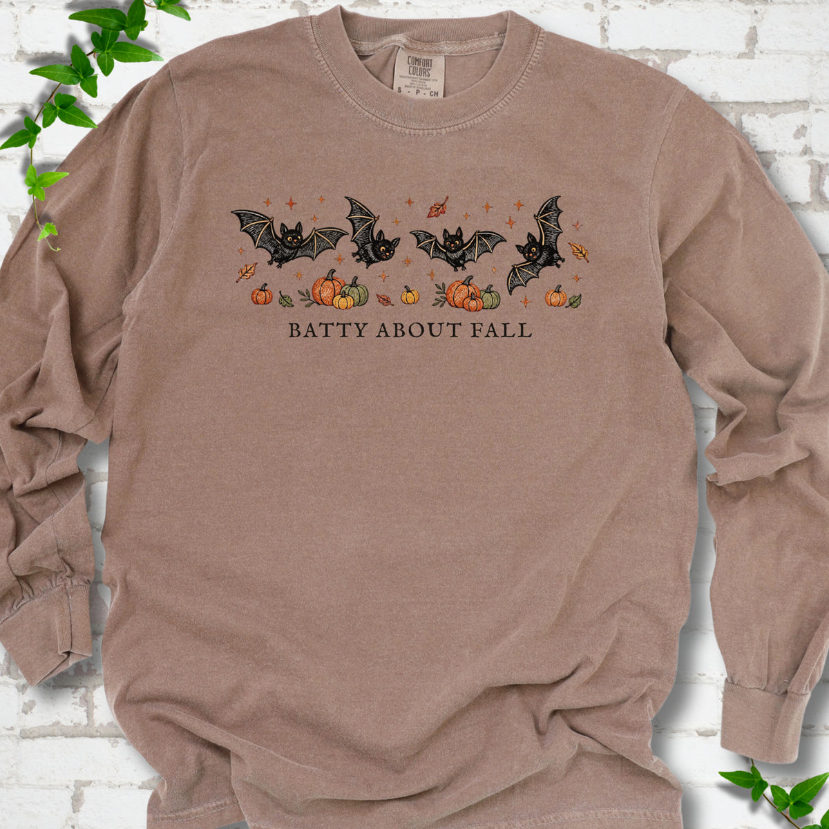 Espresso Comfort Colors® long sleeve tee flat lay featuring four black bats above pumpkins and autumn leaves with “Batty About Fall” lettering.