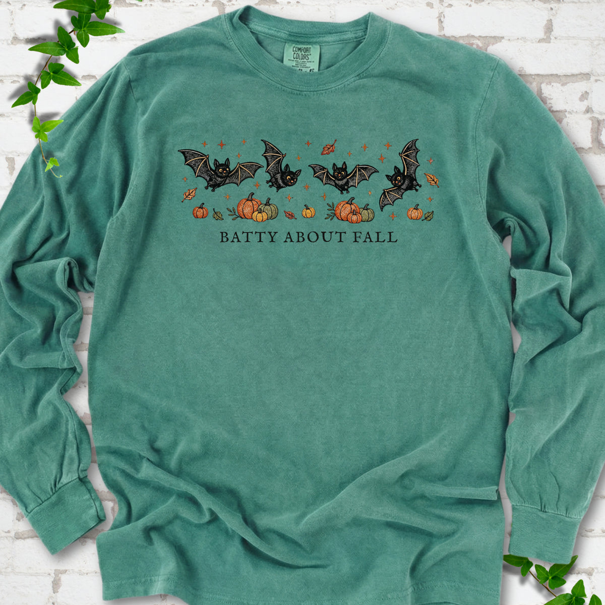 Light Green Comfort Colors® long sleeve tee flat lay featuring four black bats above pumpkins and autumn leaves with “Batty About Fall” lettering.
