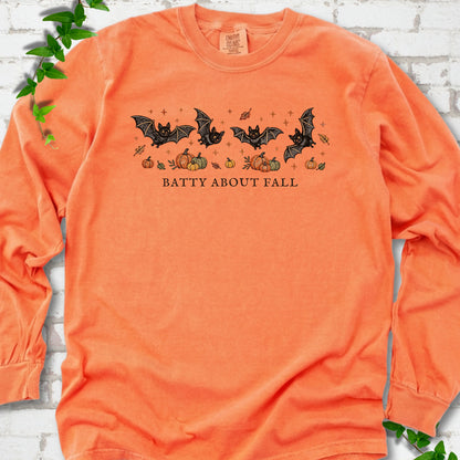 Melon Comfort Colors® long sleeve tee flat lay featuring four black bats above pumpkins and autumn leaves with “Batty About Fall” lettering.