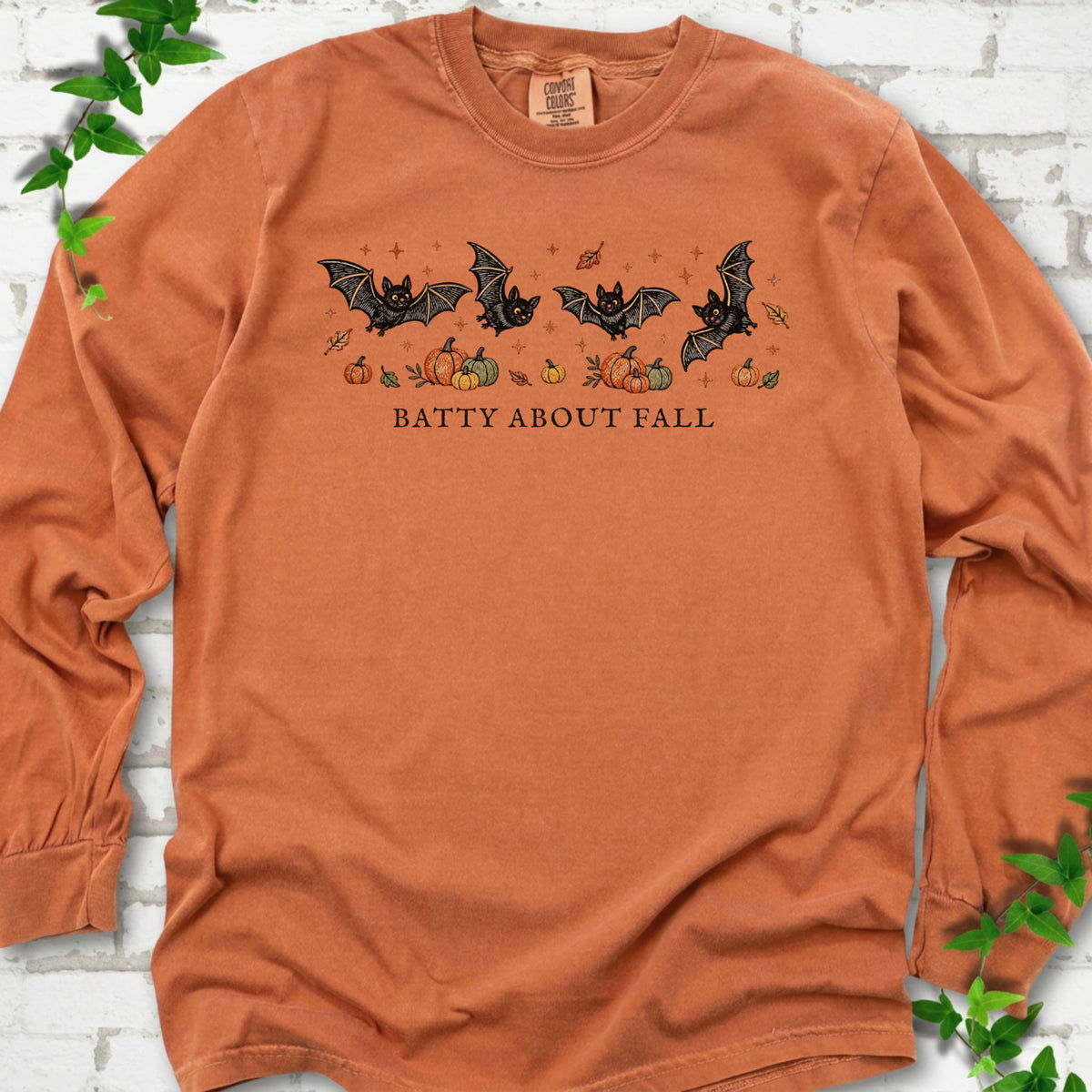 Yam Comfort Colors® long sleeve tee flat lay featuring four black bats above pumpkins and autumn leaves with “Batty About Fall” lettering.
