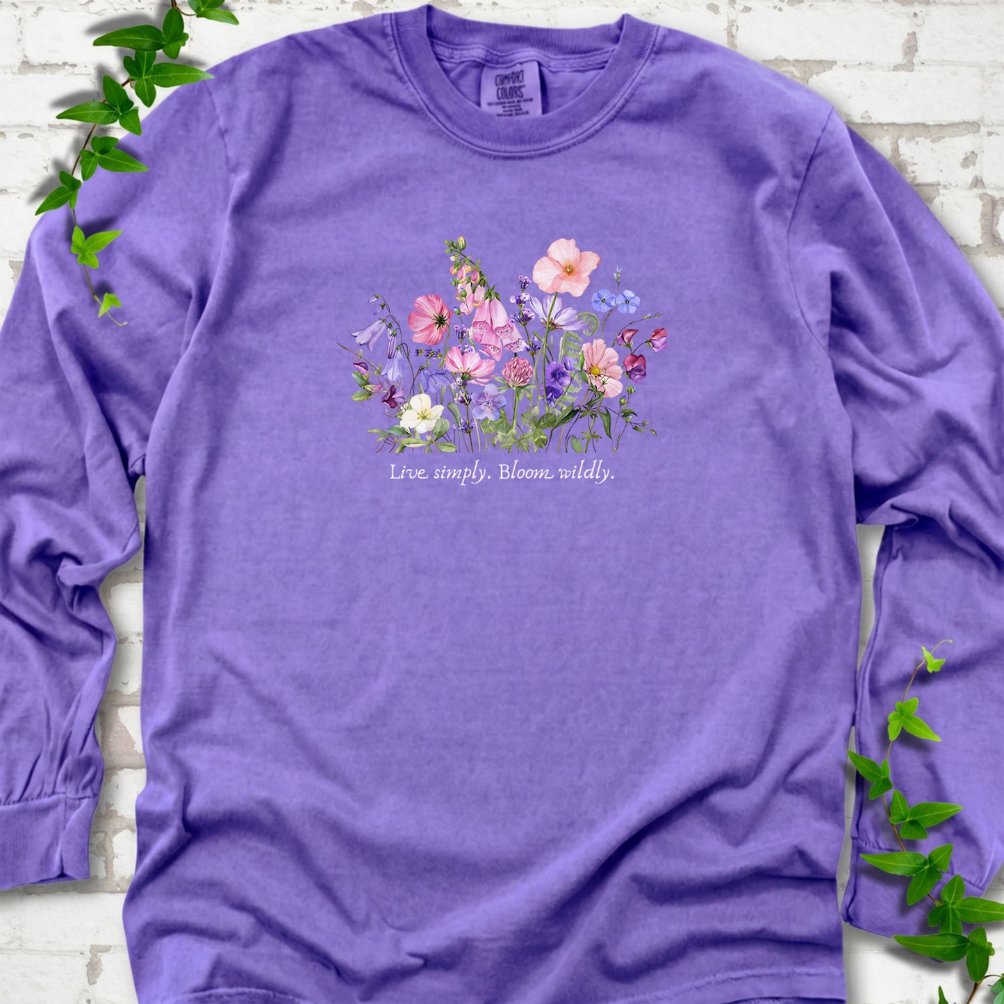 Violet Comfort Colors® long sleeve T-shirt front mockup featuring colorful wildflowers and the words “Live simply. Bloom wildly.”