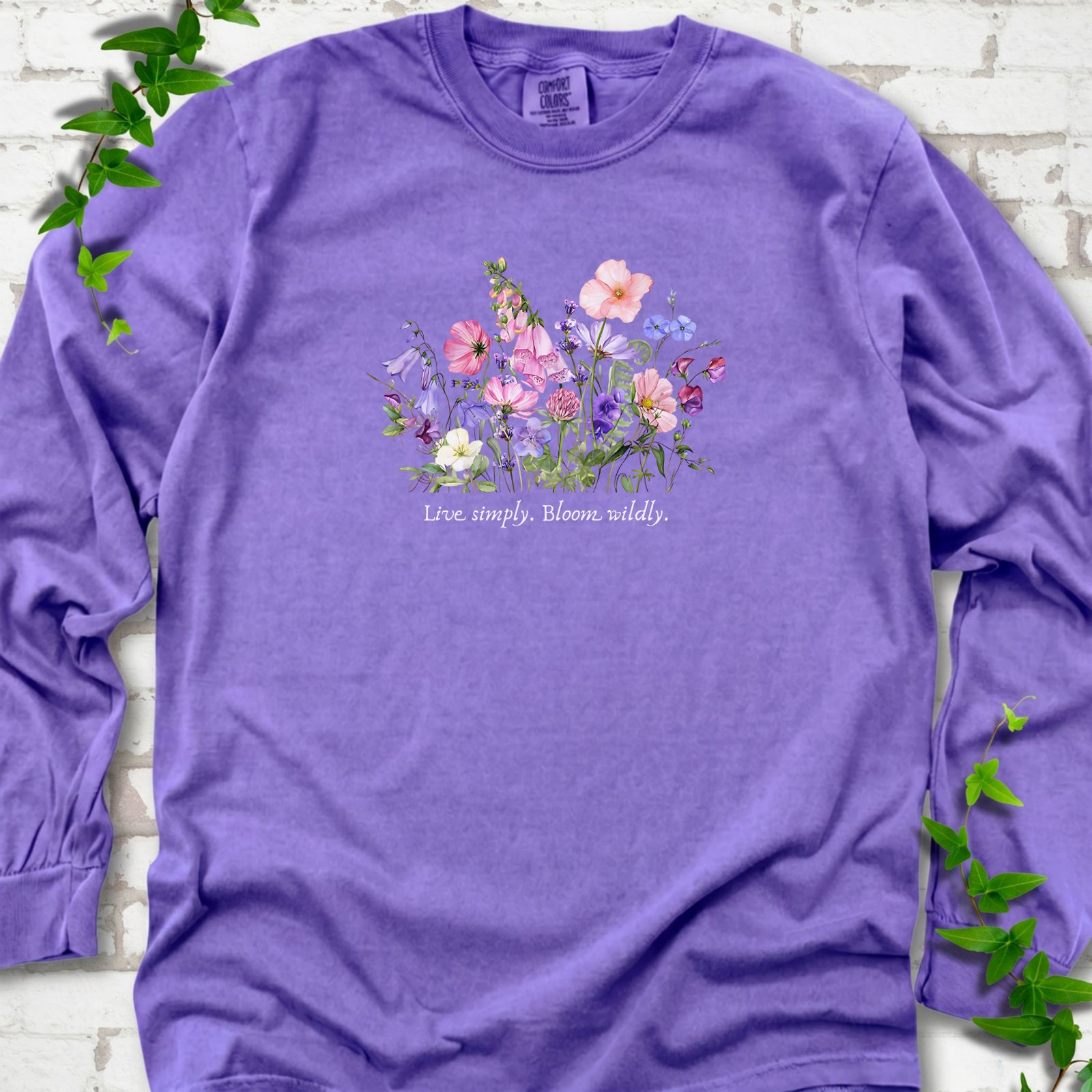 Violet Comfort Colors® long sleeve T-shirt front mockup featuring colorful wildflowers and the words “Live simply. Bloom wildly.”