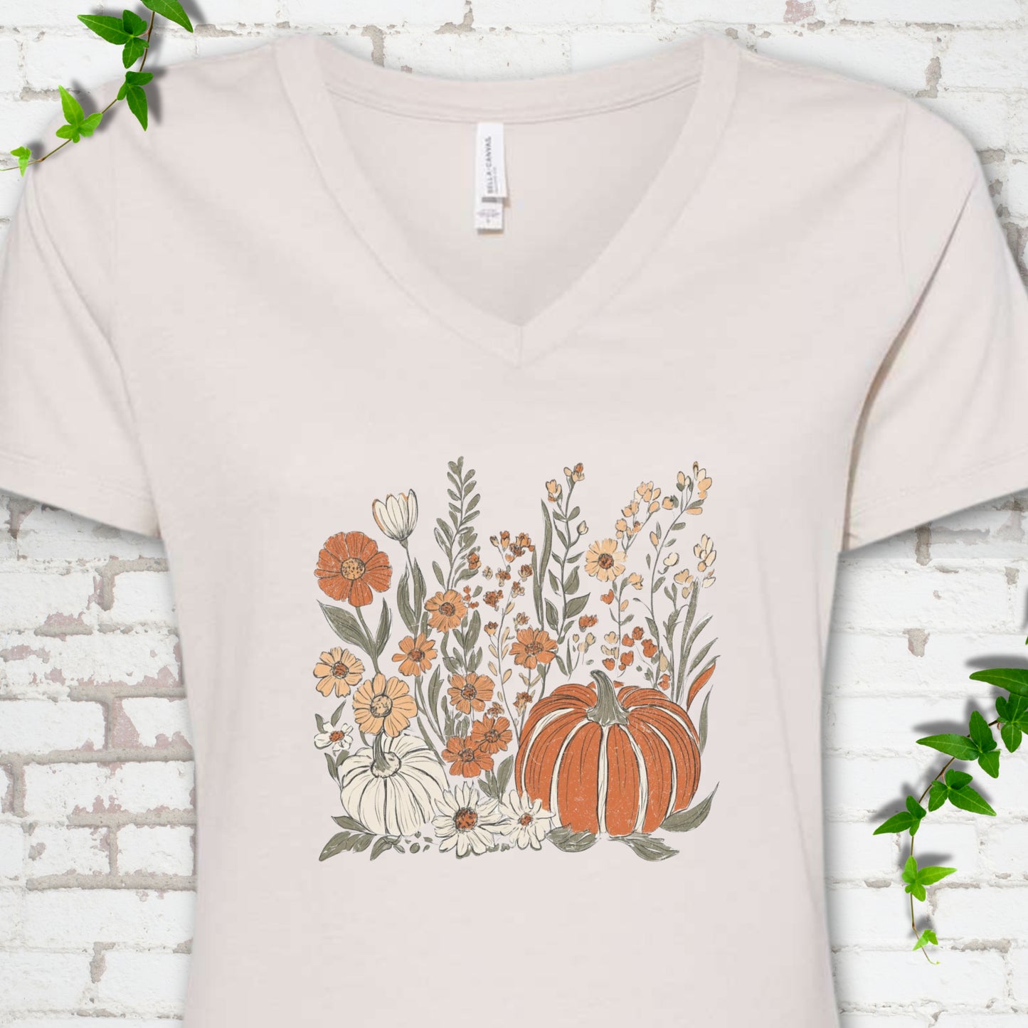 Heather Dust Bella Canvas® V-neck T-shirt flat lay featuring an orange pumpkin surrounded by cream and orange wildflowers.