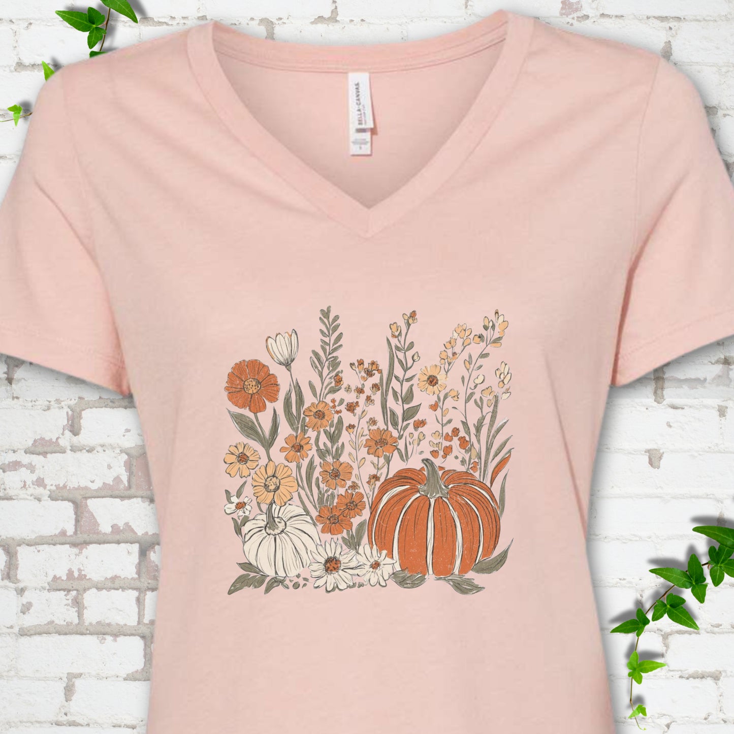 Heather Peach Bella Canvas® V-neck T-shirt flat lay featuring an orange pumpkin surrounded by cream and orange wildflowers.
