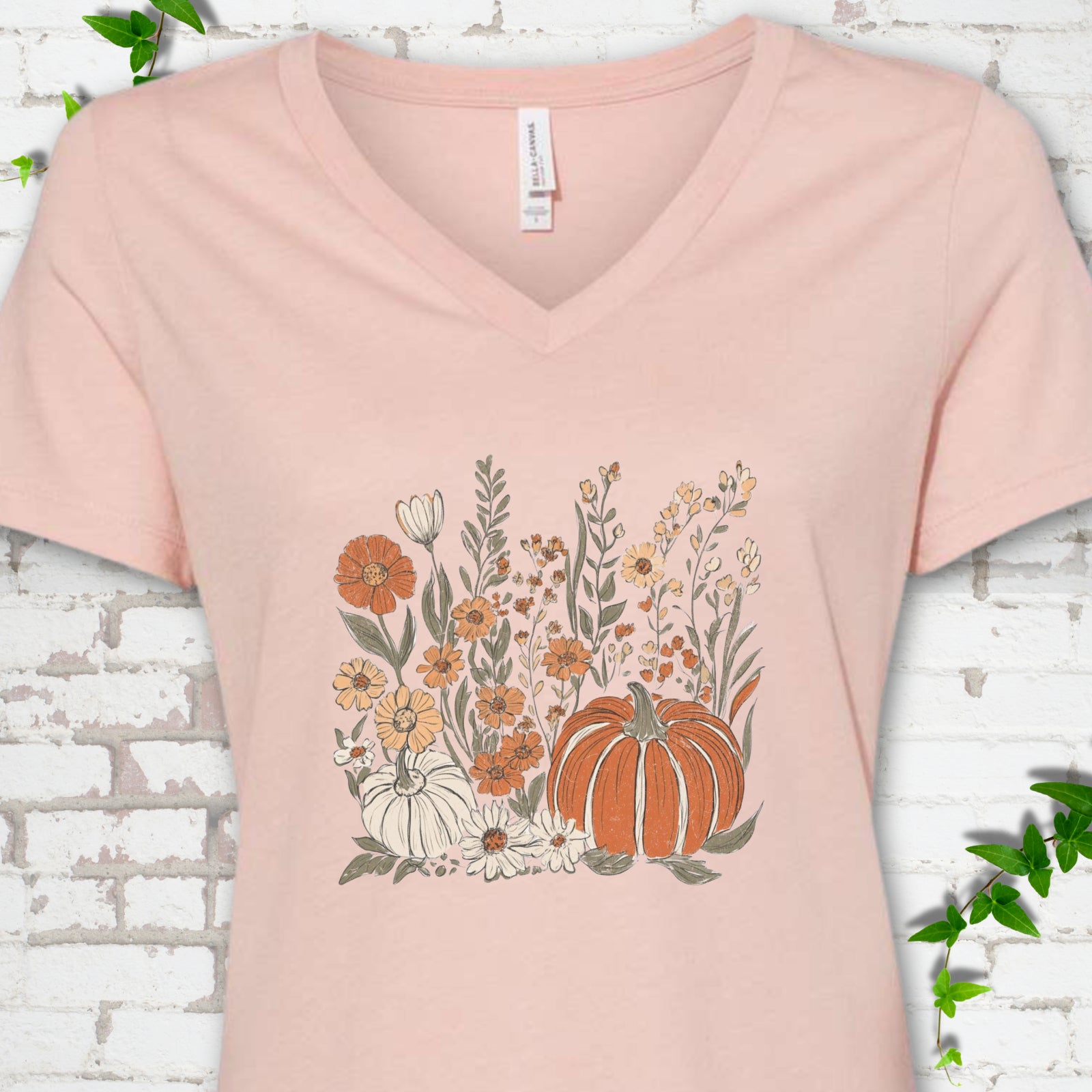 Heather Peach Bella Canvas® V-neck T-shirt flat lay featuring an orange pumpkin surrounded by cream and orange wildflowers.